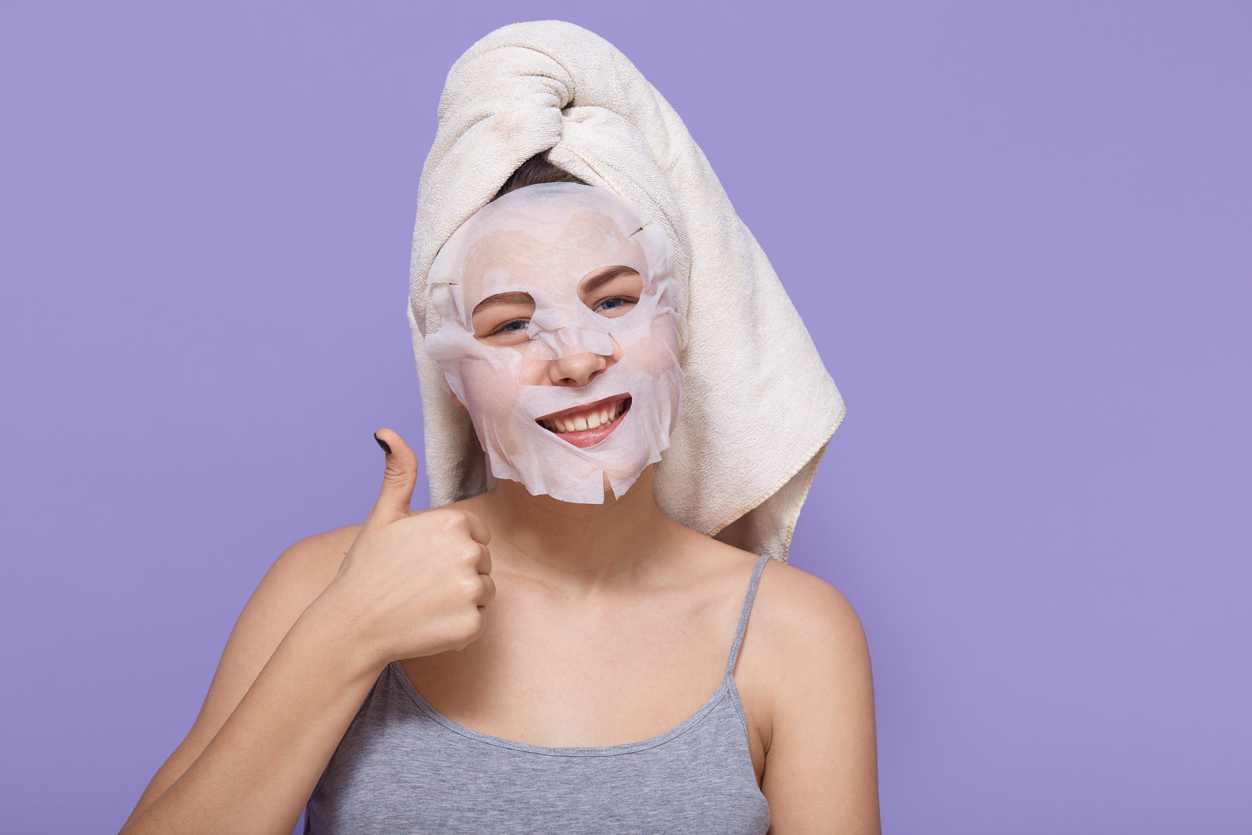 positive young woman shows her big thumb up while posing with cosmetic mask her face scaled